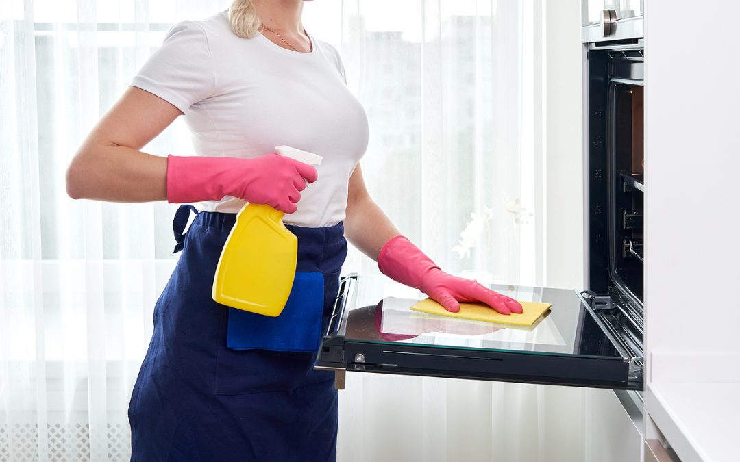 Young woman wearing gloves cleaning oven
