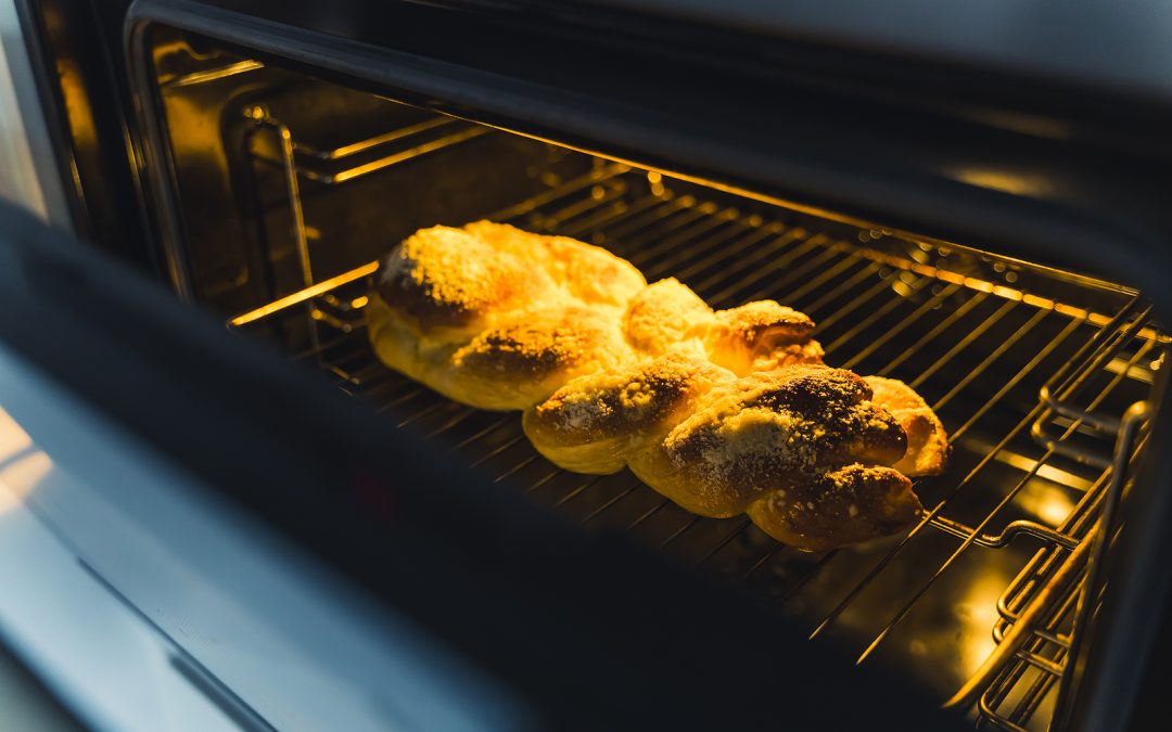 Yummy freshly-baked golden-brown Jewish challah in the oven. Baking process. Cultural and cuisine heritage. Oven door opened slightly showing the baking. High quality photo